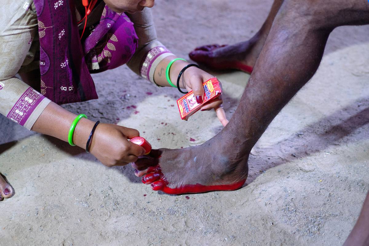 Woman applying an exfoliating foot mask for dry feet while seated on bathroom floor, smoothing gel onto heels